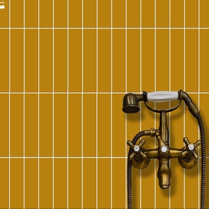 May include: A gold-toned shower faucet with a white handle and a black shower head. The faucet is mounted on a wall tiled with mustard yellow tiles.