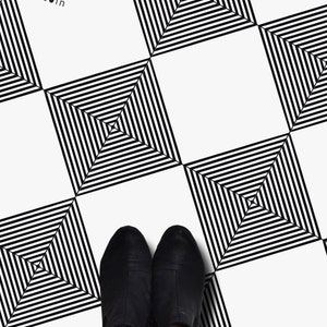 Puede incluir: Azulejos de suelo con patrón geométrico en blanco y negro con los pies de una persona que lleva botas negras de tobillo de pie sobre los azulejos.