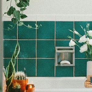 以下が含まれることがあります： 緑色のタイルで囲まれた白いバスタブ。白い花束が白い花瓶に活けられ、木製のトレイの上に置かれ、ろうそくが灯っている。手前に、鉢植えのサボテンと他の植物が置かれた木製のテーブルがある。