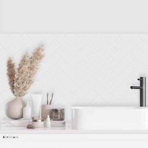 Könnte beinhalten: Weißer Badezimmer-Waschtisch mit einem weißen Porzellan-Waschbecken und einem schwarzen Wasserhahn. Der Waschtisch ist mit einer Vase mit getrocknetem Pampasgras, einer Flasche Handseife, einer Tube Handcreme, einem Tiegel Lotion, einer Flasche ätherischem Öl und einer Kerze dekoriert.