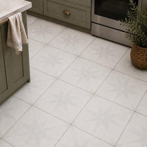 May include: Square floor tiles in a light gray finish, each featuring a centered white starburst pattern with radiating points. The tiles are arranged in a grid layout, creating a continuous geometric design across the kitchen floor surface.