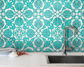May include: A kitchen backsplash featuring a repeating pattern of teal floral motifs on a white background. A stainless steel faucet is positioned over a sink, with a stack of white plates and a small white bowl sitting on the white countertop.