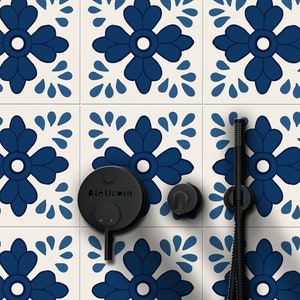 Puede incluir: Un cabezal de ducha negro y una ducha de mano con una perilla de control redonda negra etiquetada como "Bleucoin" montada en una pared de azulejos blancos con un patrón floral azul y blanco.