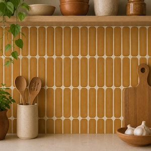 Puede incluir: Un salpicadero de cocina con azulejos verticales de color amarillo mostaza con bordes redondeados en un patrón repetitivo. La pared cuenta con un estante de madera con cuencos de cerámica, una planta, utensilios, una tabla y ajo.