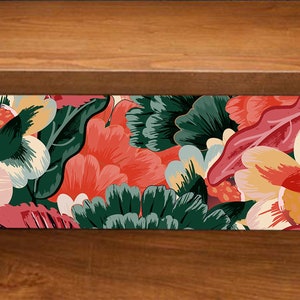 K&ouml;nnte beinhalten: Ein rechteckiger Klebeaufkleber mit einem lebendigen Blumenmuster aus gro&szlig;en, stilisierten rosa, orangefarbenen und dunkelgr&uuml;nen Bl&uuml;ten und Bl&auml;ttern. Der Aufkleber hat eine abziehbare R&uuml;ckseite mit grauer Klebefl&auml;che auf einer Holzoberfl&auml;che.