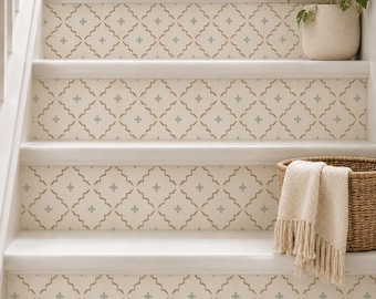Puede incluir: Una escalera con contrahuellas de color blanco roto decoradas con un patrón geométrico de celosía en color tostado y pequeñas cruces azul claro. Una cesta de mimbre con una manta de color crema con flecos descansa sobre un escalón.