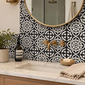 A bathroom vanity with a white marble countertop, a gold faucet, and a round gold mirror, with black and white patterned tile stickers on the wall.