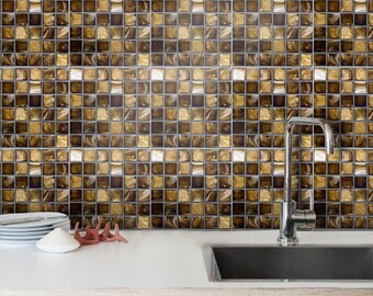 May include: A kitchen backsplash featuring a grid of square tiles in shades of metallic gold, bronze, and dark brown. The tiles have a reflective, glossy finish and are arranged in a repeating pattern. A silver faucet is positioned over a sink.