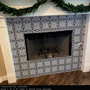 A fireplace with a black screen and white mantel, with the area around the firebox covered in black and white patterned tile stickers.