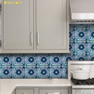 Könnte beinhalten: Ein Küchenspiegel mit quadratischen Fliesen, die ein sich wiederholendes geometrisches Blumenmuster in Blau, Weiß und Dunkeltürkis aufweisen. Die Fliesen sind zwischen hellgrauen Küchenschränken und einer weißen Arbeitsplatte angebracht.