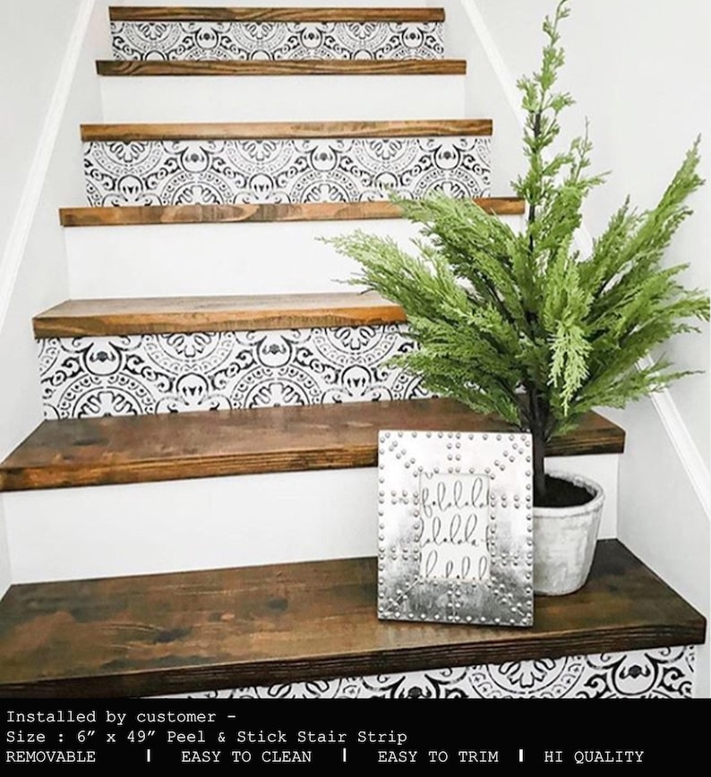 A staircase with dark wood treads and white risers covered in black and white patterned decals, with a small faux Christmas tree and a silver studded sign on the first step.