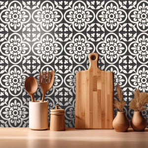 A kitchen counter with a wooden cutting board, utensils in a ceramic holder, and dried plants in vases, against a wall covered in black and white patterned tile stickers.