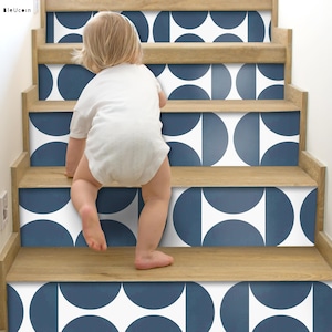 Puede incluir: Un niño pequeño se arrastra por un tramo de escaleras con calcomanías de patrones geométricos azules y blancos. Las calcomanías están en un patrón repetitivo de semicírculos.