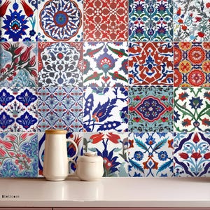 Op de afbeelding: Een verzameling decoratieve keramische tegels met ingewikkelde bloemen- en geometrische patronen in blauw, rood en wit. Een witte kan en een kleine pot staan voor de tegels. De tegels zijn in een raster gerangschikt.