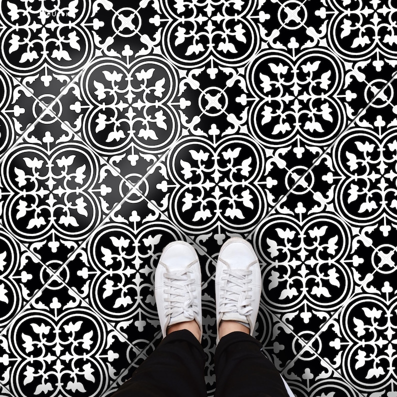 May include: A black and white floor tile pattern featuring a repeating symmetrical floral motif. The design consists of intricate white scrollwork and leaf shapes set against a solid black background, creating a high-contrast geometric grid.