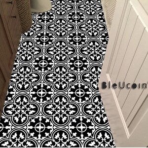 May include: A floor covering featuring a repeating black and white geometric pattern with circular and floral motifs. The design includes a series of interconnected shapes across the surface. The text BleUcoin is visible on the right side.