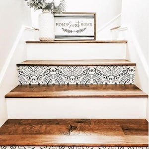 A staircase with dark wood treads and white risers covered in black and white patterned decals, with a white vase of flowers and a "Home Sweet Home" sign on the first step.