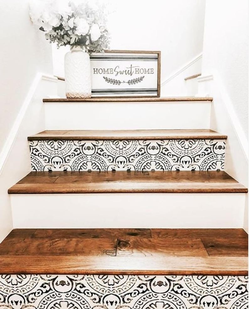 A staircase with dark wood treads and white risers covered in black and white patterned decals, with a white vase of flowers and a "Home Sweet Home" sign on the first step.