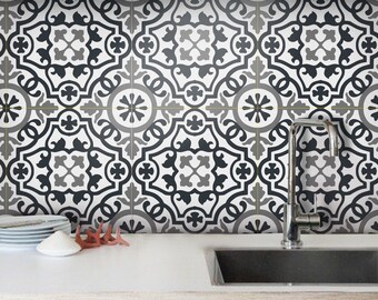 May include: A kitchen backsplash featuring square tiles with a repeating black, white, and gray geometric pattern. The wall is positioned behind a white countertop, a stainless steel sink, and a metal faucet. The text BleUcoin is visible.