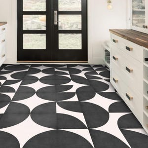 May include: Geometric black and white floor tiles. The design features a repeating pattern of semi-circles and triangles. The tiles create a modern look. The floor is in a room with white cabinets and a black door.
