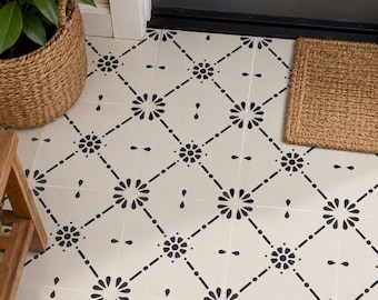 May include: A square floor tile featuring a white base with a black stenciled pattern of repeating diamond shapes, small floral motifs at each intersection, and teardrop accents, creating a continuous geometric design across the surface.