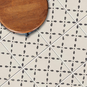May include: A wooden, round tabletop with a dark finish is partially visible in the upper left corner. The background features off-white tiles with a repeating pattern of dark gray floral designs. The tiles are arranged in a grid.