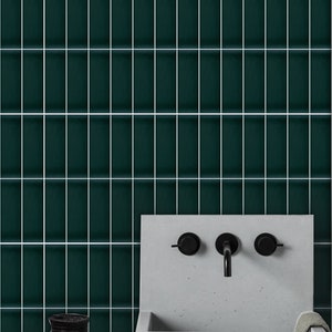 May include: A dark green tiled wall with white grout lines. A white concrete sink with a black faucet and two black knobs is in the lower right corner of the image. A black and white patterned vase and a woven basket are on the counter in the lower left corner.