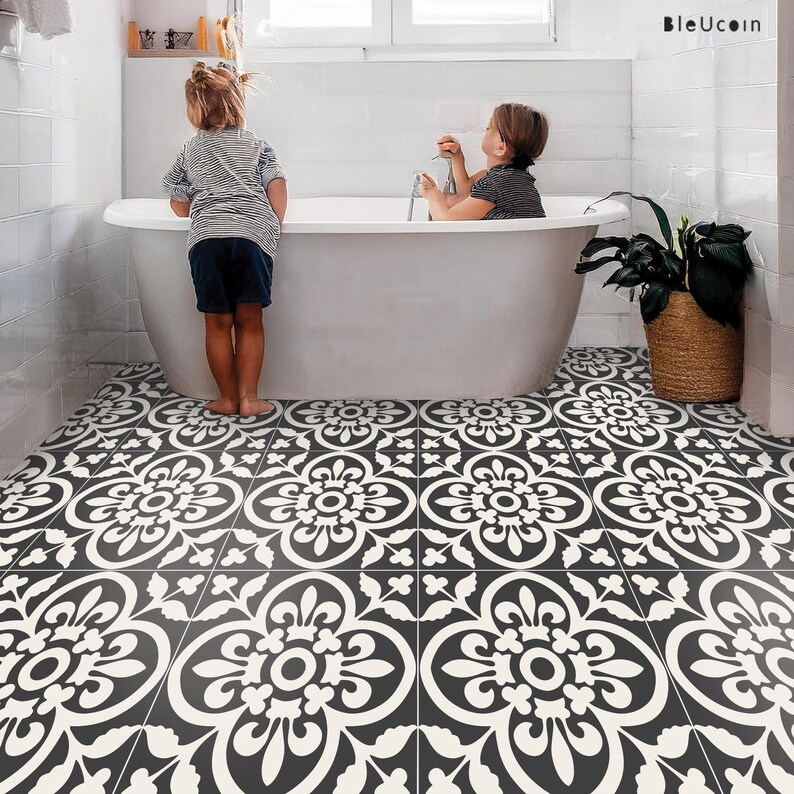 Two children in a bathroom with a white freestanding tub, with the floor covered in black and white patterned tile stickers.