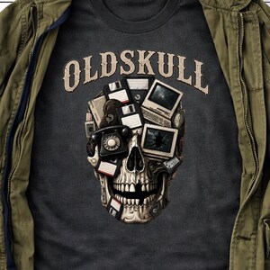 Peut inclure: Un t-shirt gris foncé avec un motif de crâne composé de technologies vintage, incluant des disquettes, un téléphone à cadran et des écrans d'ordinateur. Le texte "OLDSKULL" est imprimé en beige dans une police arquée au-dessus du crâne.