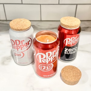May include: Three Dr Pepper-branded candles, one in a white can labeled "Diet", one in a red can labeled "Zero Sugar", and one in a red can labeled "23" with a red and white cork lid.