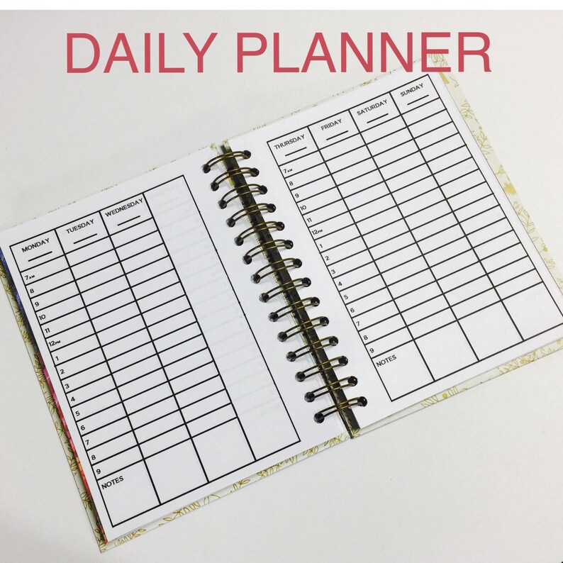 May include: A daily planner with a gold and white floral design. The planner has a spiral binding and is open to show the weekly schedule. The days of the week are listed across the top of the page, and the hours of the day are listed down the side. There is a section for notes at the bottom of each page.