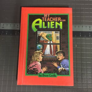 May include: A paperback book titled "MY TEACHER is an ALIEN" by Bruce Coville. The cover features a green alien teacher in a window, with two children looking on in surprise. The book has a red border.