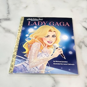May include: A Little Golden Book biography of Lady Gaga. The cover features a colorful illustration of Lady Gaga singing into a microphone. The text on the cover reads "a Little Golden Book" and "Lady Gaga".