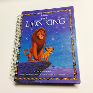 May include: A spiral-bound book titled Disney's The Lion King, featuring an illustration of an adult lion and a lion cub standing on a rock against a starry blue night sky. The cover includes text by Gina Ingoglia and illustrators Marshall Toomey and Michael Humphries.