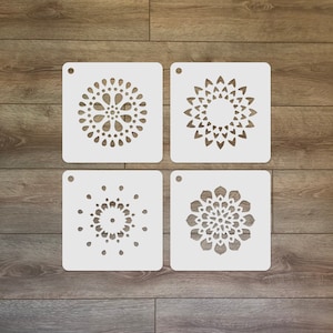 May include: Four white plastic stencils with different mandala designs. Each stencil has a hole in the top for hanging.