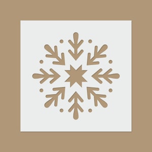 Op de afbeelding: Een witte papieren sneeuwvlok uitsnijding met een bruine ster in het midden. De sneeuwvlok heeft een eenvoudig ontwerp met zes punten en een cirkel van kleine stippen rond de buitenkant.