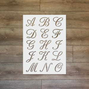 Può includere: Un foglio di stencil bianco con le lettere dell'alfabeto in un carattere corsivo. Le lettere sono disposte in tre righe di cinque lettere ciascuna.