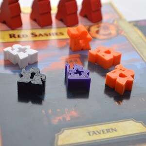 May include: A game board with various colored plastic game pieces. The board has the words "Red Sashes", "Tavern", and "Active Quests" printed on it. The game pieces are red, white, orange, purple, and black.