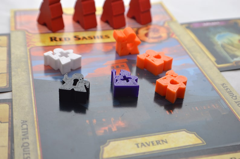 May include: A game board with various colored plastic game pieces. The board has the words "Red Sashes", "Tavern", and "Active Quests" printed on it. The game pieces are red, white, orange, purple, and black.