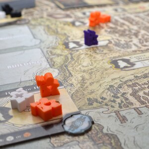 May include: A game board with a map of a fictional land. There are small plastic figures in orange, white, purple and black. The board has text that says "Building" and "Castle Waterdeep".