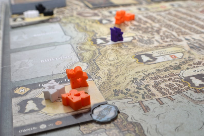 May include: A game board with a map of a fictional land. There are small plastic figures in orange, white, purple and black. The board has text that says "Building" and "Castle Waterdeep".