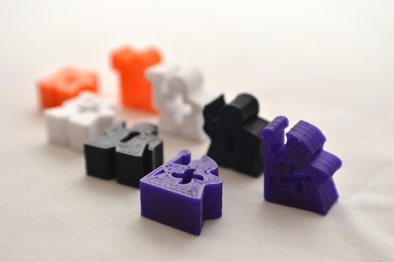 May include: A set of seven miniature 3D printed houses in various colors, including orange, white, black, and purple. The houses are all different shapes and sizes, and some have intricate details.