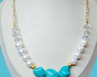 May include: A gold chain necklace with a combination of white pearls, clear crystal beads, and turquoise stones. The necklace is displayed on a white mannequin bust against a light blue background.