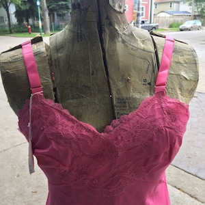 Può includere: Un sottoveste di raso rosa con bordino in pizzo. Il sottoveste è su un manichino con un motivo.