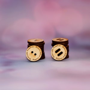 May include: Two wooden buttons with the text "Removable PomPom - Remove before washing" printed around the edge. One button has two holes, the other has a long slot.