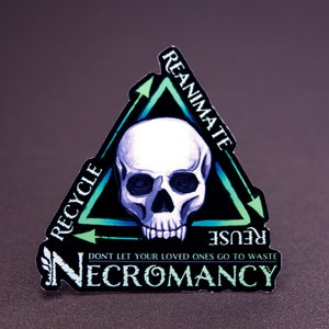May include: A black and green sticker with a skull in the center and the words "REANIMATE", "REUSE", "RECYCLE" and "NECROMANCY" around it. The sticker is shaped like a triangle with arrows pointing in a circular motion.