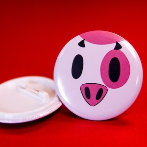 Peut inclure: Bouton blanc avec un visage de cochon de dessin animé rose et noir. Le cochon a un nez rose et une tache rose sur le visage.