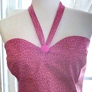 May include: A pink halter top with a leopard print design. The top features a sweetheart neckline and a halter strap that connects at the neck with a small pink ball. The fabric has a repeating pattern of dark pink spots.