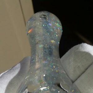 May include: A clear glass pipe with rainbow glitter and star charms. The pipe is white and has a round, bulbous shape.