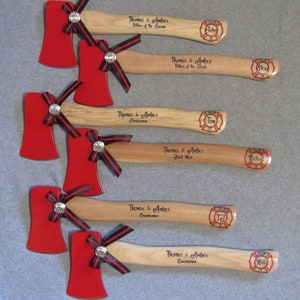 May include: Six red and black miniature axes with wooden handles. Each axe has a personalized inscription and a fire department logo with a name on it. The inscriptions include "Thomas & Amber", "Father of the Groom", "Father of the Bride", "Best Man", "Groomsman", and "Bridesman".